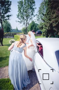 Die Trauzeugin hilft der Braut beim Einsteigen in das Hochzeitsauto Brautauto